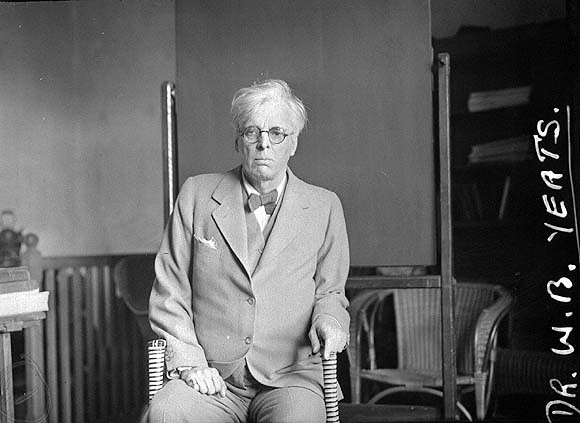 W.B. Yeats sitting on a chair with a walking stick in hand