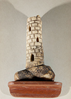 Photograph of a round tower carved in bone mounted on a wooden plinth.